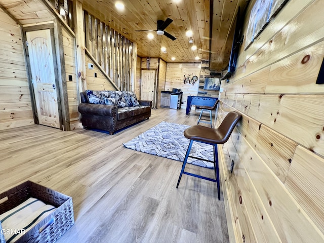 living room featuring wooden walls, light hardwood / wood-style flooring, ceiling fan, and wooden ceiling