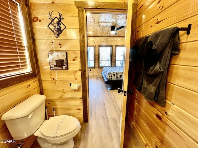 bathroom with hardwood / wood-style flooring, ceiling fan, wood walls, and toilet