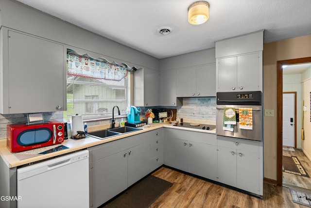 kitchen with stainless steel oven, white dishwasher, sink, decorative backsplash, and light wood-type flooring