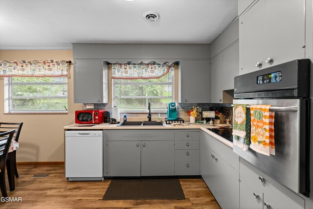 kitchen with white dishwasher, oven, light hardwood / wood-style floors, and sink