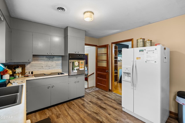 kitchen featuring wall oven, tasteful backsplash, hardwood / wood-style flooring, gray cabinets, and white fridge with ice dispenser