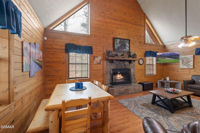 living room featuring hardwood / wood-style flooring, ceiling fan, a textured ceiling, a stone fireplace, and wood walls