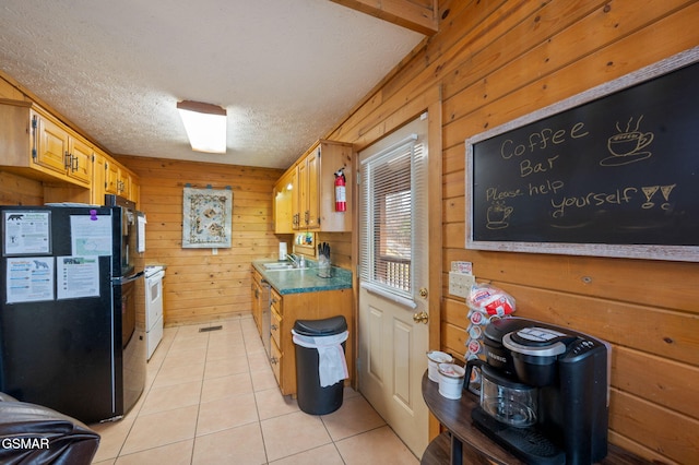 kitchen with black refrigerator, sink, wood walls, and light tile patterned floors