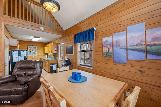 dining space with high vaulted ceiling, wooden walls, and light hardwood / wood-style floors