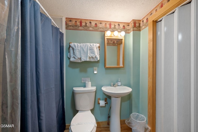 bathroom with a shower with shower curtain, toilet, sink, and a textured ceiling