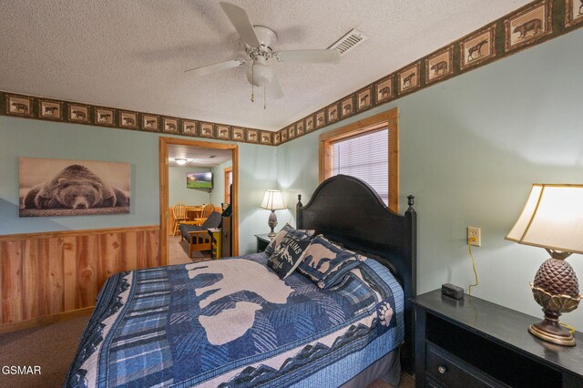 carpeted bedroom with ceiling fan, a textured ceiling, and wood walls