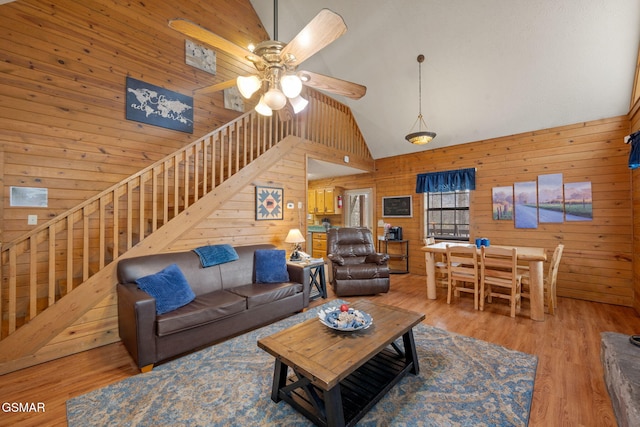 living room with wood-type flooring, high vaulted ceiling, ceiling fan, and wood walls