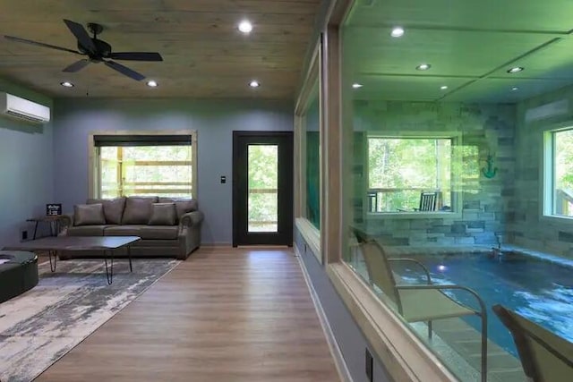 living room with ceiling fan, an AC wall unit, plenty of natural light, and light wood-type flooring