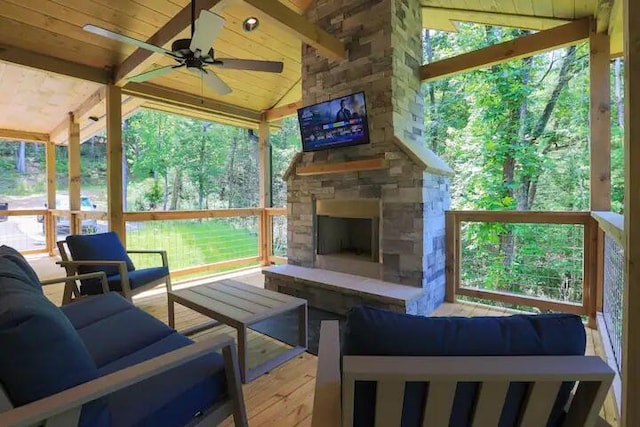 unfurnished sunroom featuring ceiling fan, lofted ceiling with beams, wooden ceiling, and an outdoor stone fireplace