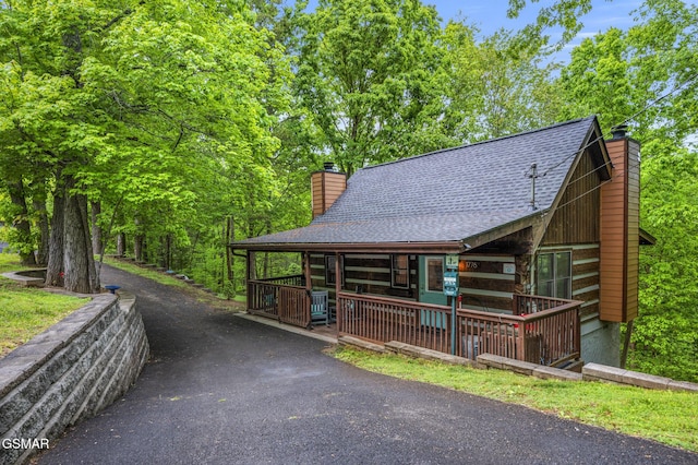 view of front of home featuring aphalt driveway, a chimney, a porch, and roof with shingles