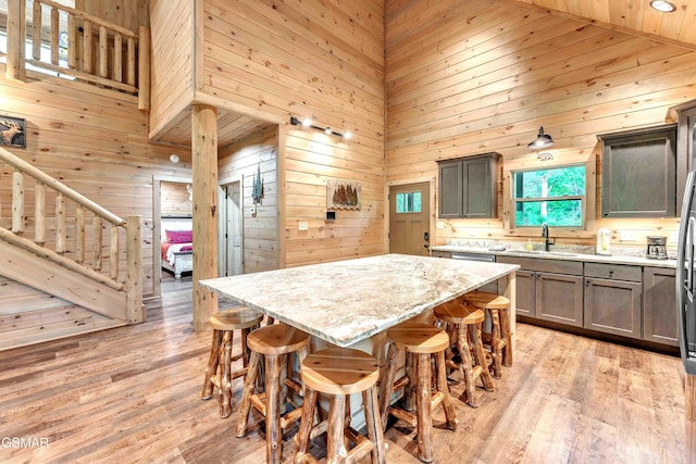 kitchen with high vaulted ceiling, a sink, wooden walls, light stone countertops, and a kitchen breakfast bar