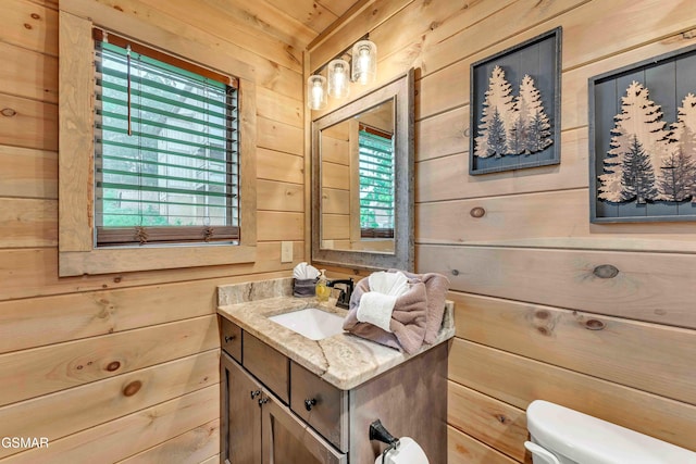 bathroom with wood walls, toilet, plenty of natural light, and vanity