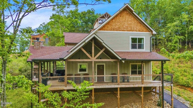 rear view of property with board and batten siding, roof with shingles, a chimney, and a porch
