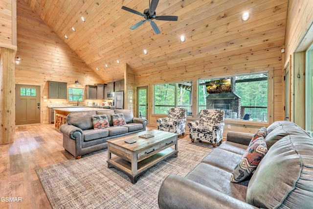 living room with healthy amount of natural light, a ceiling fan, wood ceiling, wood walls, and light wood-style floors