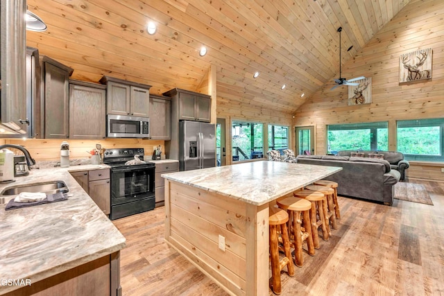kitchen with appliances with stainless steel finishes, high vaulted ceiling, a sink, a center island, and a kitchen breakfast bar