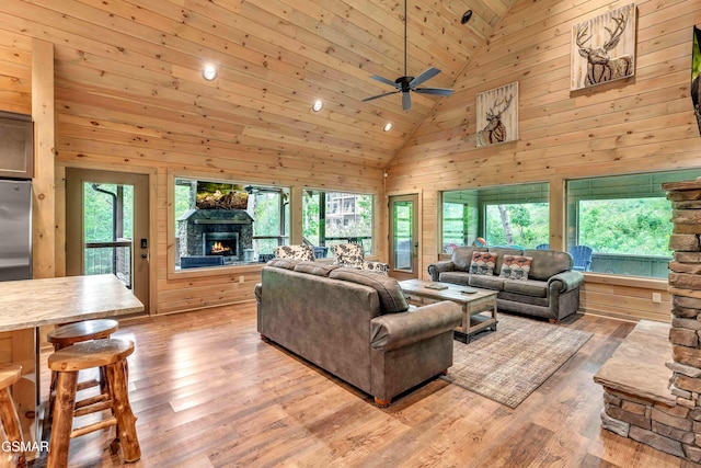 living area featuring a fireplace, high vaulted ceiling, light wood-style flooring, wooden walls, and a ceiling fan