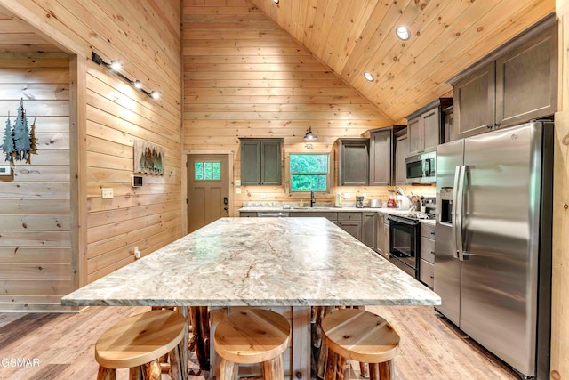 kitchen featuring appliances with stainless steel finishes, wood ceiling, a center island, a breakfast bar area, and light wood-style flooring