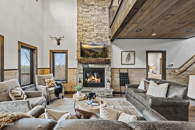 living room with a high ceiling, wood walls, a fireplace, and light hardwood / wood-style floors