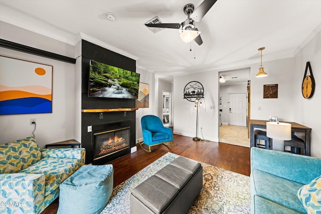 living room featuring ceiling fan, a large fireplace, dark hardwood / wood-style flooring, and crown molding