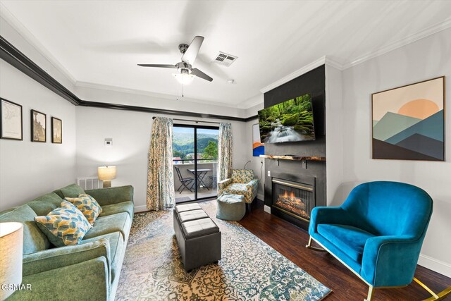 living room featuring crown molding, a large fireplace, ceiling fan, and dark hardwood / wood-style floors