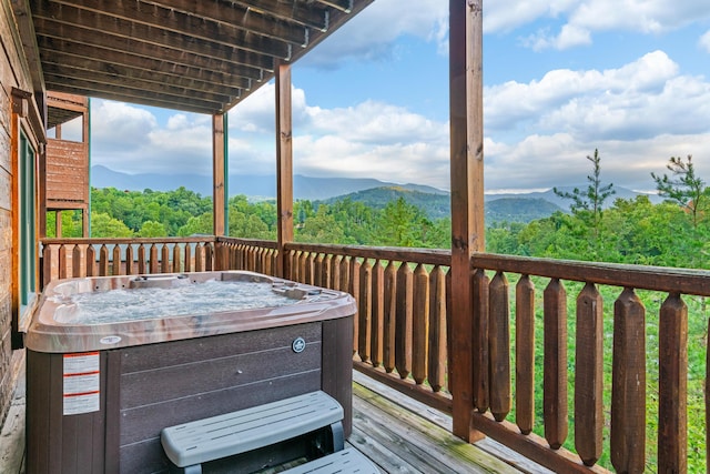 wooden terrace with a view of trees, a hot tub, and a mountain view