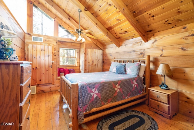 bedroom with ceiling fan, vaulted ceiling with beams, light hardwood / wood-style floors, wooden walls, and wood ceiling