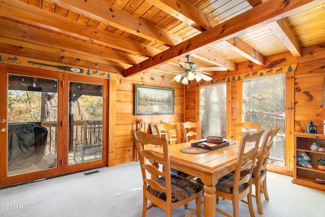 carpeted dining room featuring beam ceiling, ceiling fan, wooden walls, and wood ceiling