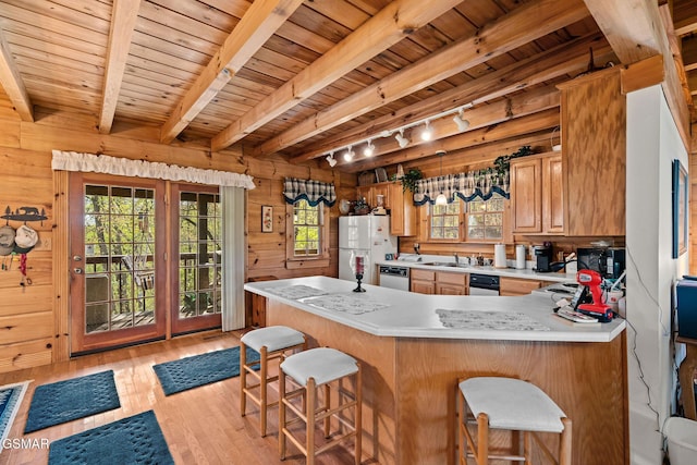 kitchen featuring light wood finished floors, track lighting, wooden walls, white appliances, and light countertops