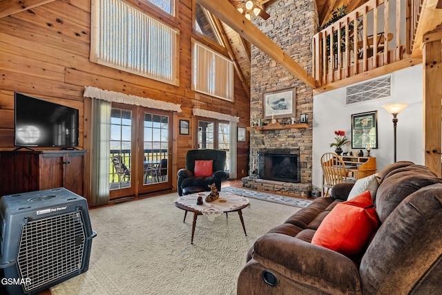 carpeted living room featuring a stone fireplace, a high ceiling, wood walls, and french doors