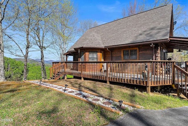 back of house featuring a deck with mountain view, roof with shingles, and a lawn