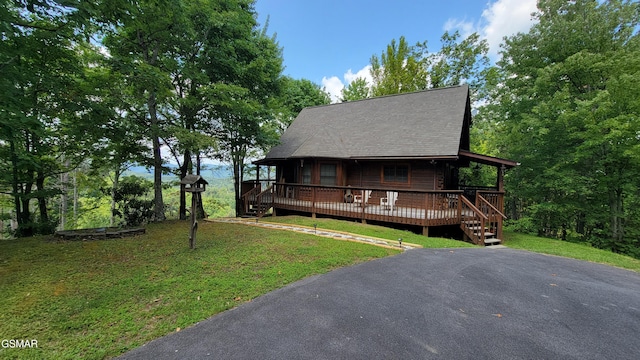 view of front of house featuring a wooden deck, a shingled roof, and a front yard