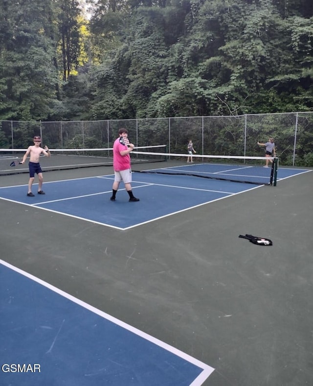 view of sport court with fence, a view of trees, and community basketball court