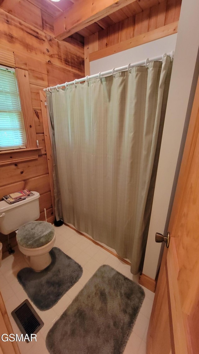 bathroom with visible vents, a shower with shower curtain, toilet, beamed ceiling, and wood walls