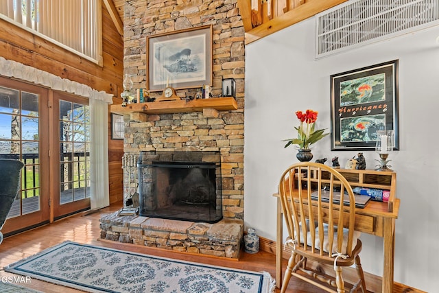 interior space with a stone fireplace, a towering ceiling, hardwood / wood-style flooring, and wood walls