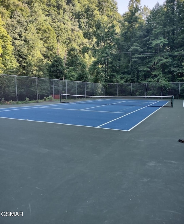view of sport court with a view of trees and fence