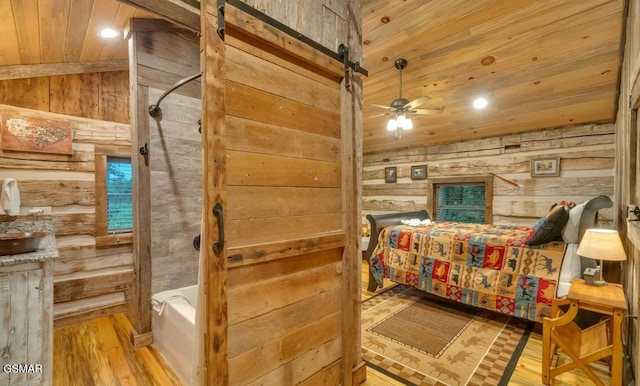 bedroom with a barn door, wooden walls, wood ceiling, and light wood-type flooring