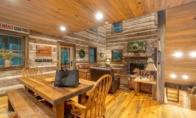 dining area featuring a stone fireplace, wooden walls, wooden ceiling, and light hardwood / wood-style floors