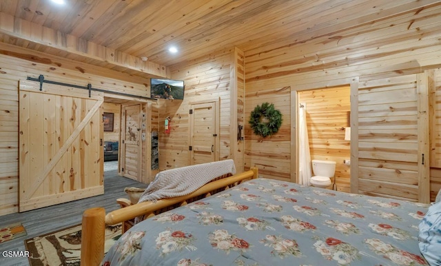 bedroom featuring ensuite bathroom, a barn door, and wooden walls