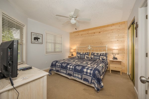 carpeted bedroom with a textured ceiling, ceiling fan, and wood walls