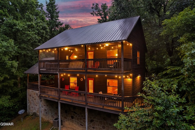 back house at dusk featuring a wooden deck, a balcony, and central AC