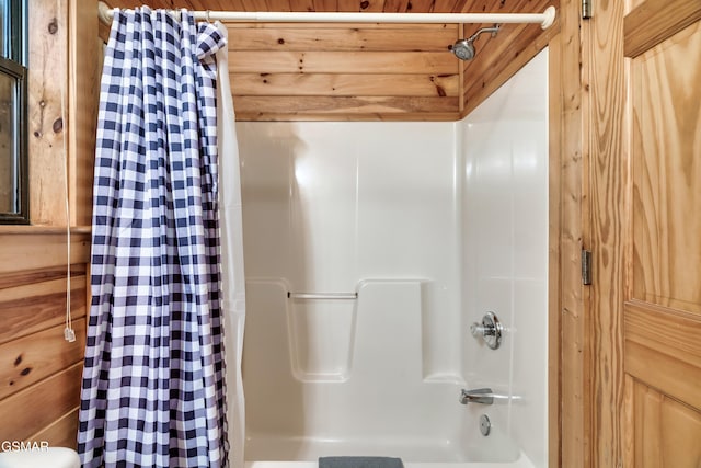 bathroom with wooden walls and shower / tub combo