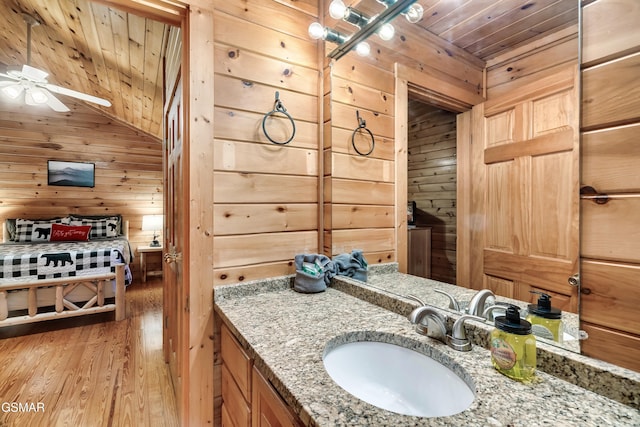 bathroom with wood-type flooring, wooden ceiling, vanity, wooden walls, and ceiling fan