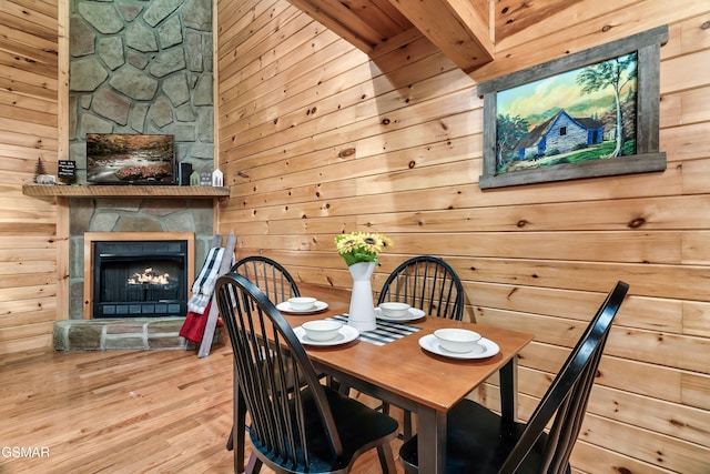 dining room with wooden walls, a stone fireplace, and light hardwood / wood-style flooring