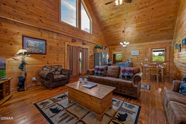 living room with high vaulted ceiling, ceiling fan with notable chandelier, wood walls, wood ceiling, and wood-type flooring