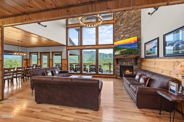 living area featuring light wood finished floors, a chandelier, wood ceiling, a fireplace, and a towering ceiling