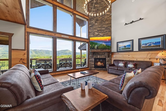 living area with a wainscoted wall, wood walls, a stone fireplace, an inviting chandelier, and wood finished floors