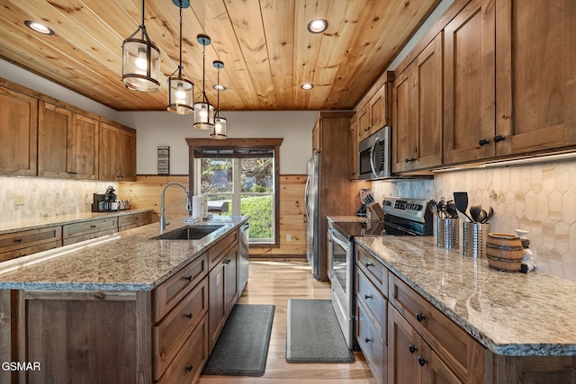 kitchen featuring brown cabinets, an island with sink, a sink, stainless steel appliances, and wood ceiling