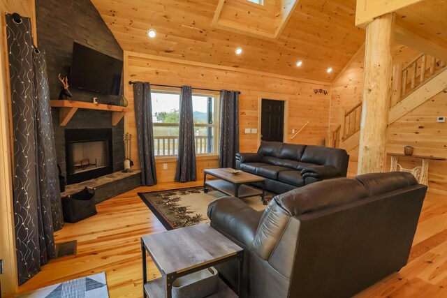 living room featuring wooden walls, high vaulted ceiling, wooden ceiling, a fireplace, and light hardwood / wood-style floors