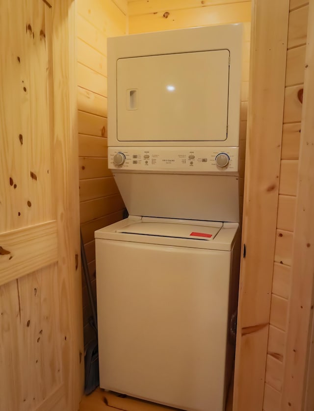 laundry area featuring wood walls and stacked washer and dryer