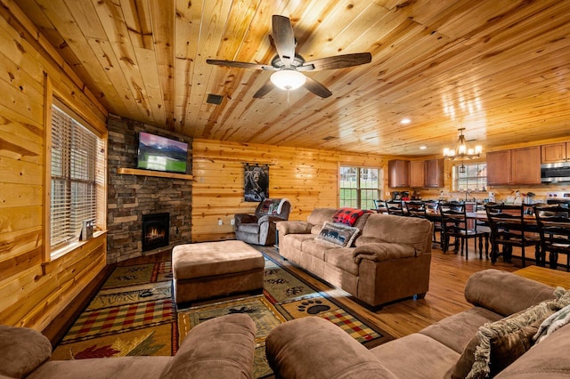 living room with wood walls, a stone fireplace, ceiling fan with notable chandelier, wooden ceiling, and wood finished floors